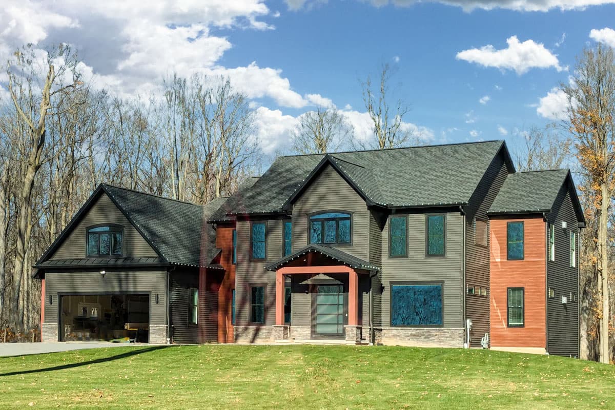 House plan exterior with two stories, gabled roof, and attached garage. Features include a front entry porch and mixed siding materials.