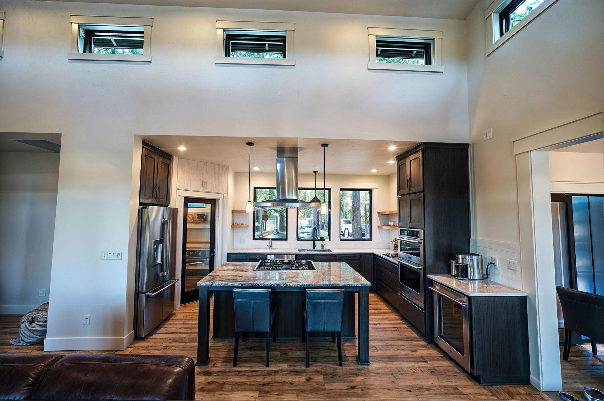 Modern kitchen with island, stainless steel appliances, dark wood cabinetry, and clerestory windows.