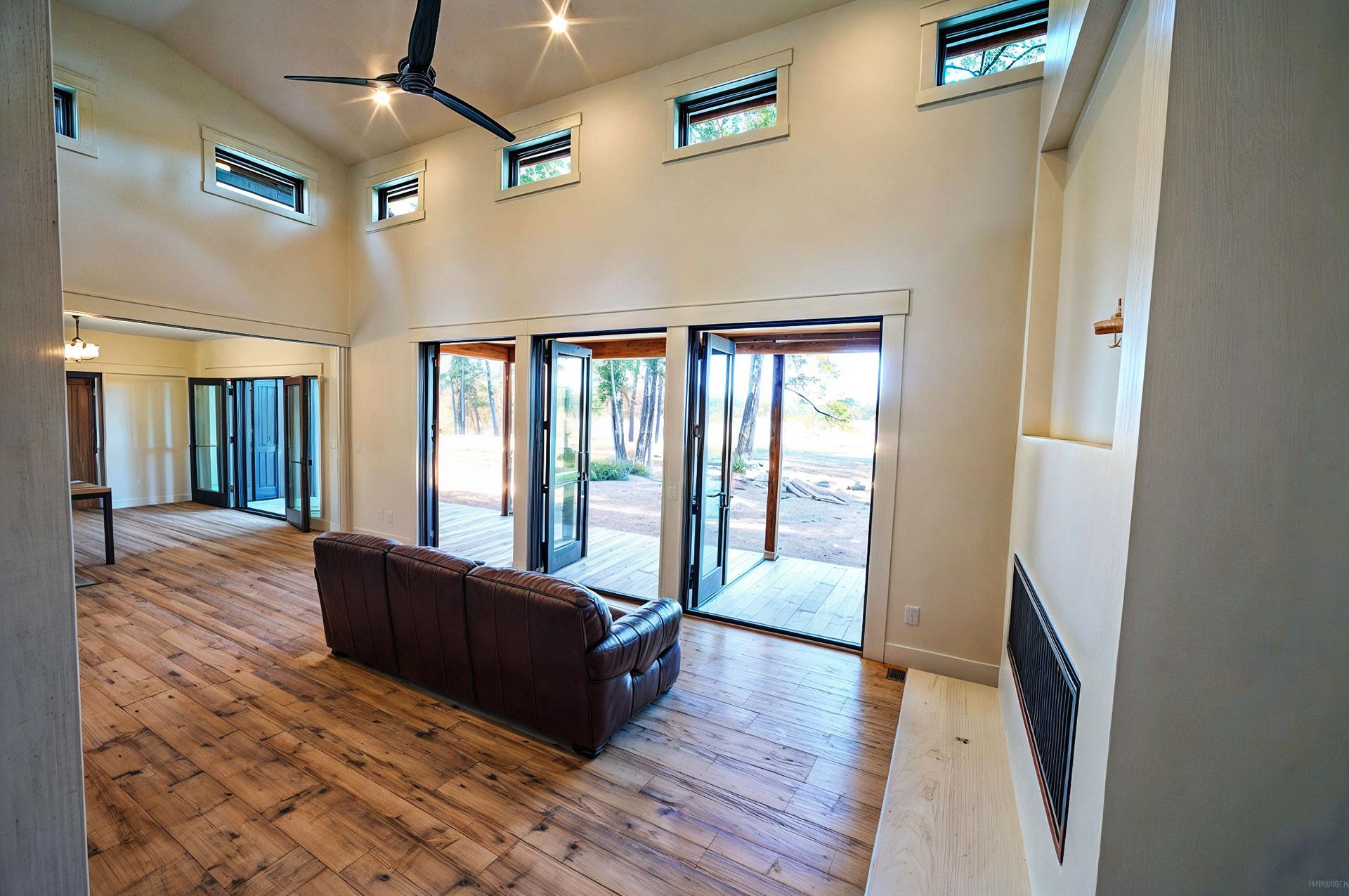 Interior view of great room with vaulted ceiling, large sliding glass doors, and natural wood flooring.