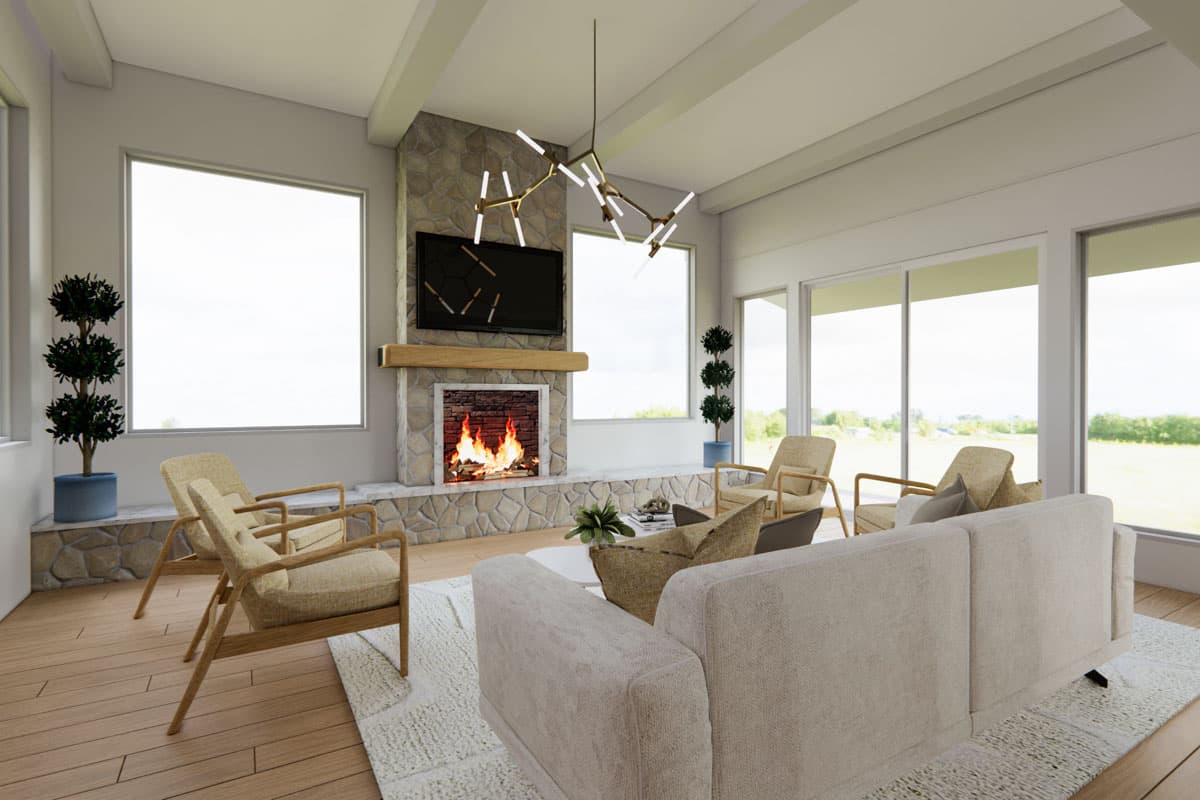 A modern living room with a stone fireplace, a lit fire, and a mounted TV. Beige sofa, chairs, and large windows overlook a green landscape.