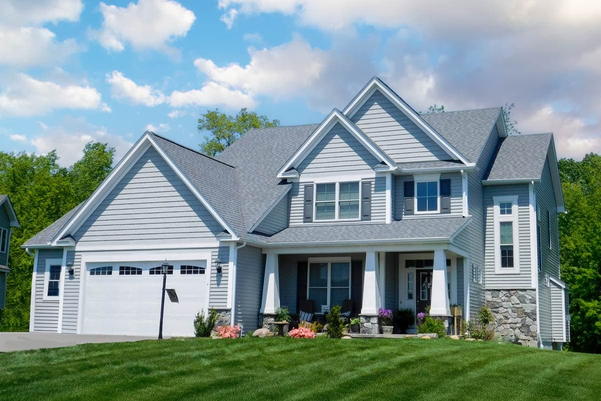 Two-story house plan exterior with a gabled roof, front porch with columns, and a side-entry garage. Features include stone accents.