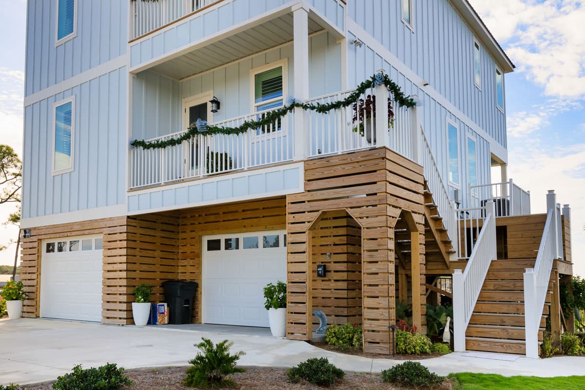 House plan exterior: Three-story building with board and batten siding, two garages, and a covered balcony with white railing.
