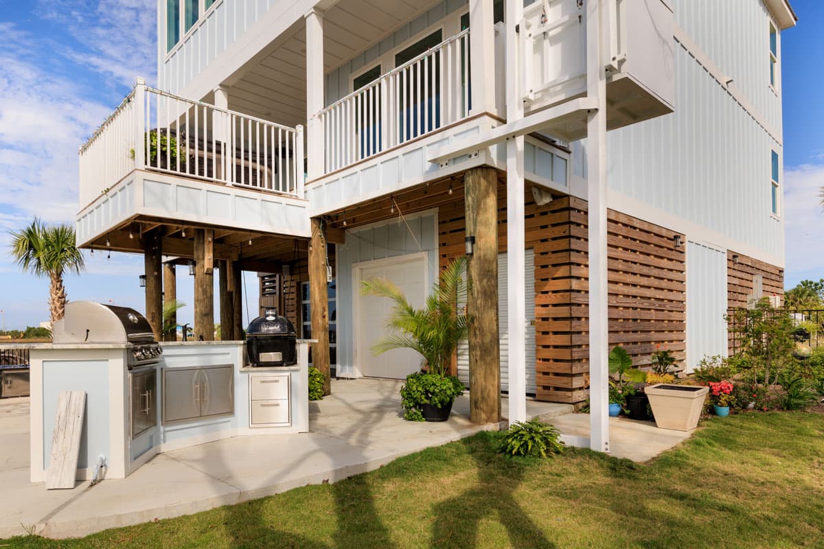 House plan exterior: two-story elevated coastal home with covered decks, outdoor kitchen, and wooden slat siding.