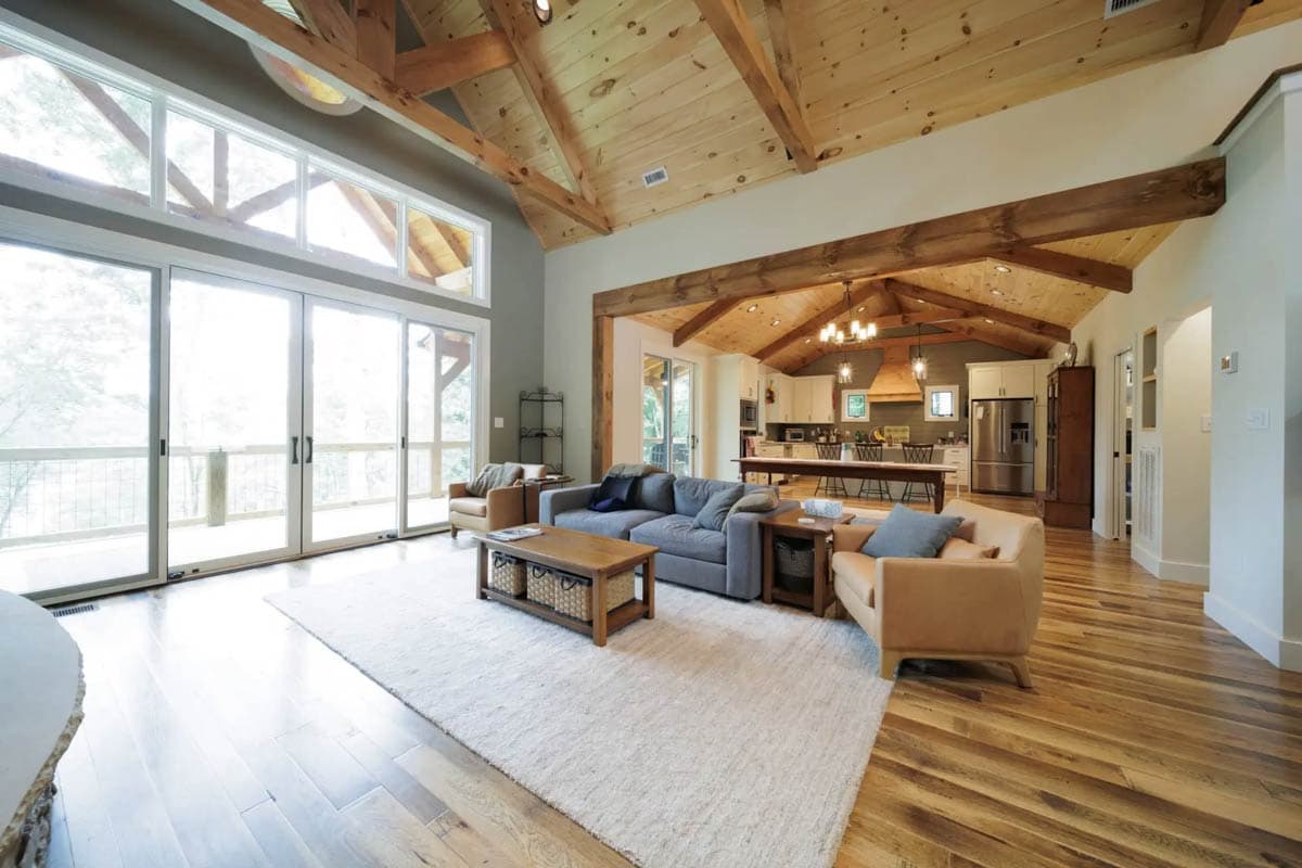 Open-concept great room with vaulted wood-beamed ceiling, large windows, and adjacent kitchen.