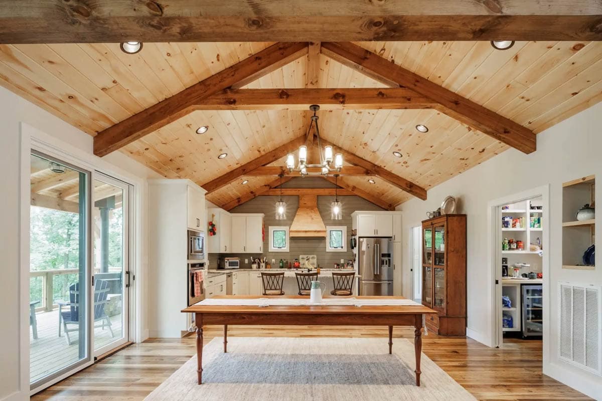 Open-concept kitchen and dining area with vaulted wood beam ceiling, island, and large sliding glass doors to deck.