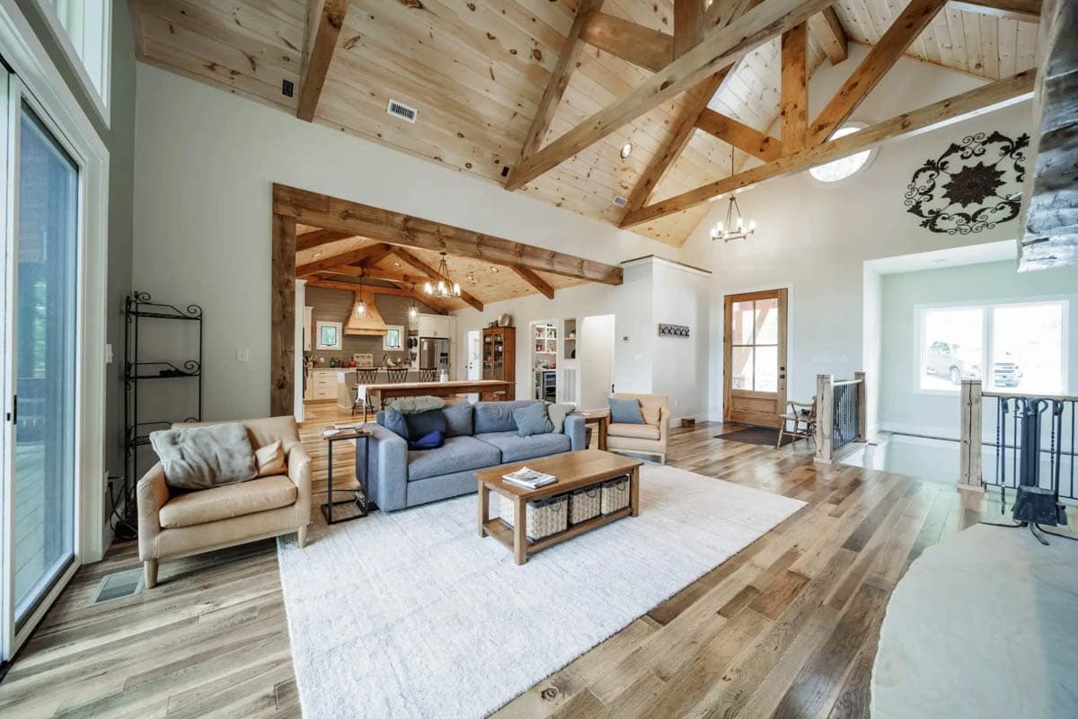 Open concept living area with vaulted wood-beamed ceiling, exposed trusses, and view into kitchen.