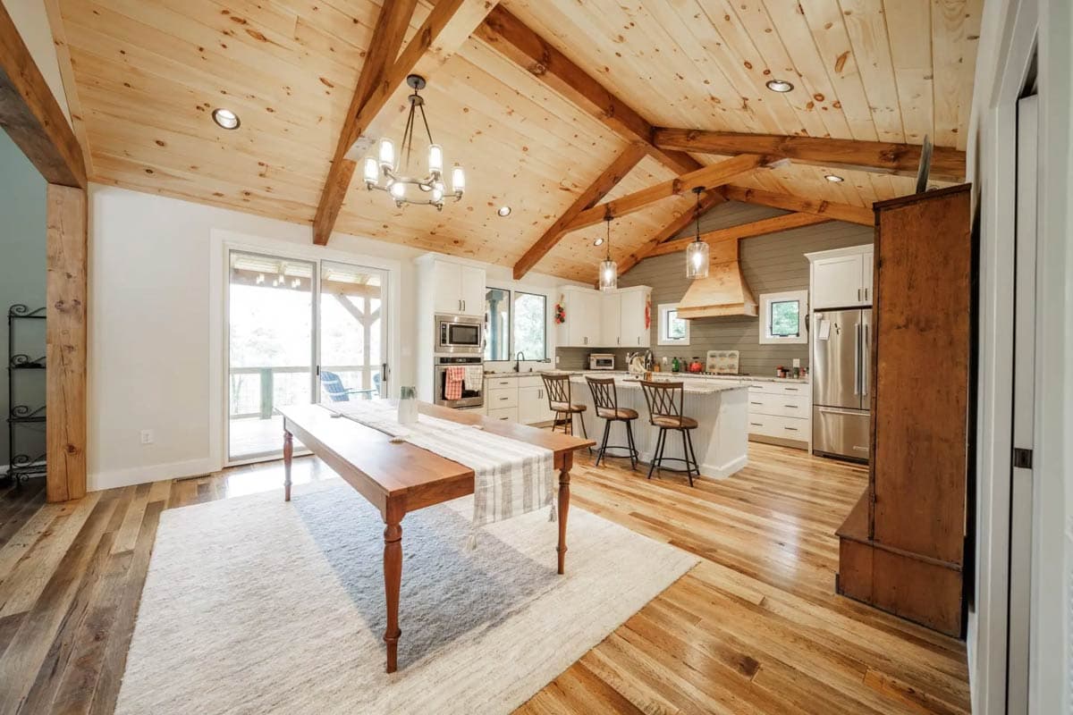 Open-concept kitchen and dining area featuring vaulted wood-beamed ceiling, island with seating, and sliding glass doors.