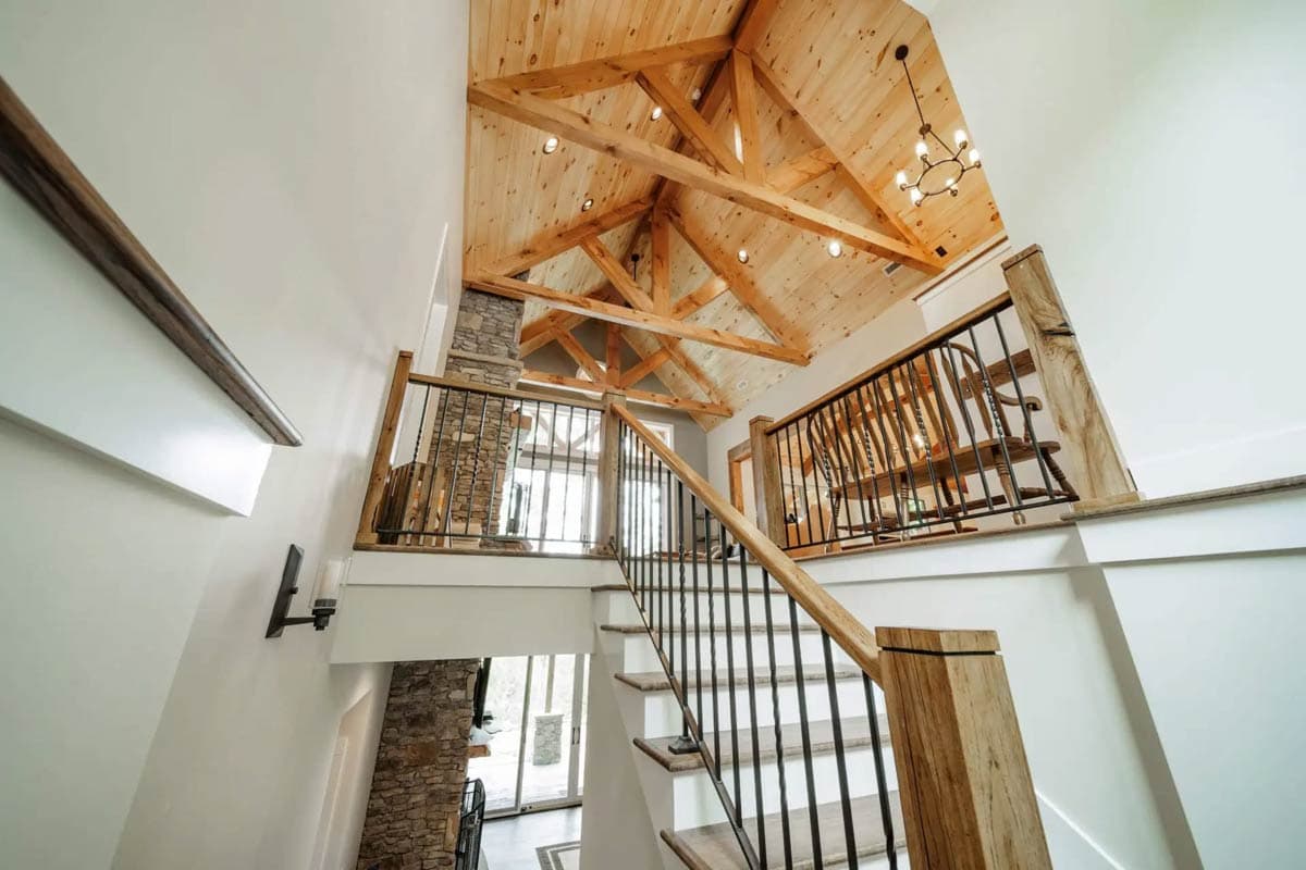 Interior view of grand staircase with vaulted, wood-paneled ceiling, exposed beams, stone fireplace, and metal railings.