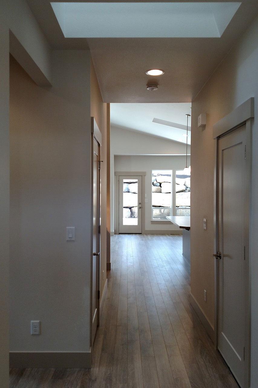 Interior view of hallway leading to a great room with vaulted ceiling, skylight, and stone exterior windows.
