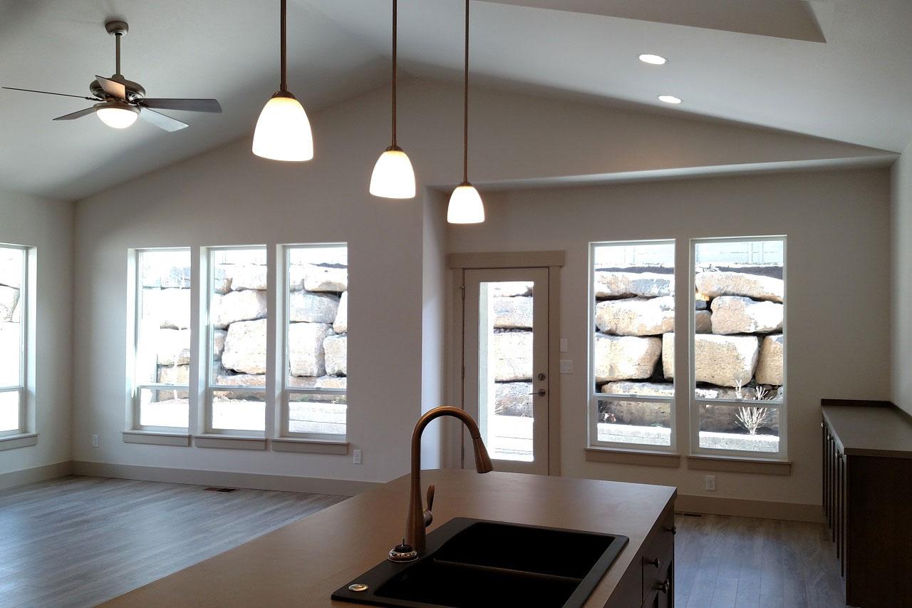 Interior view of a room with vaulted ceiling, pendant lights, and large windows overlooking a rock wall.