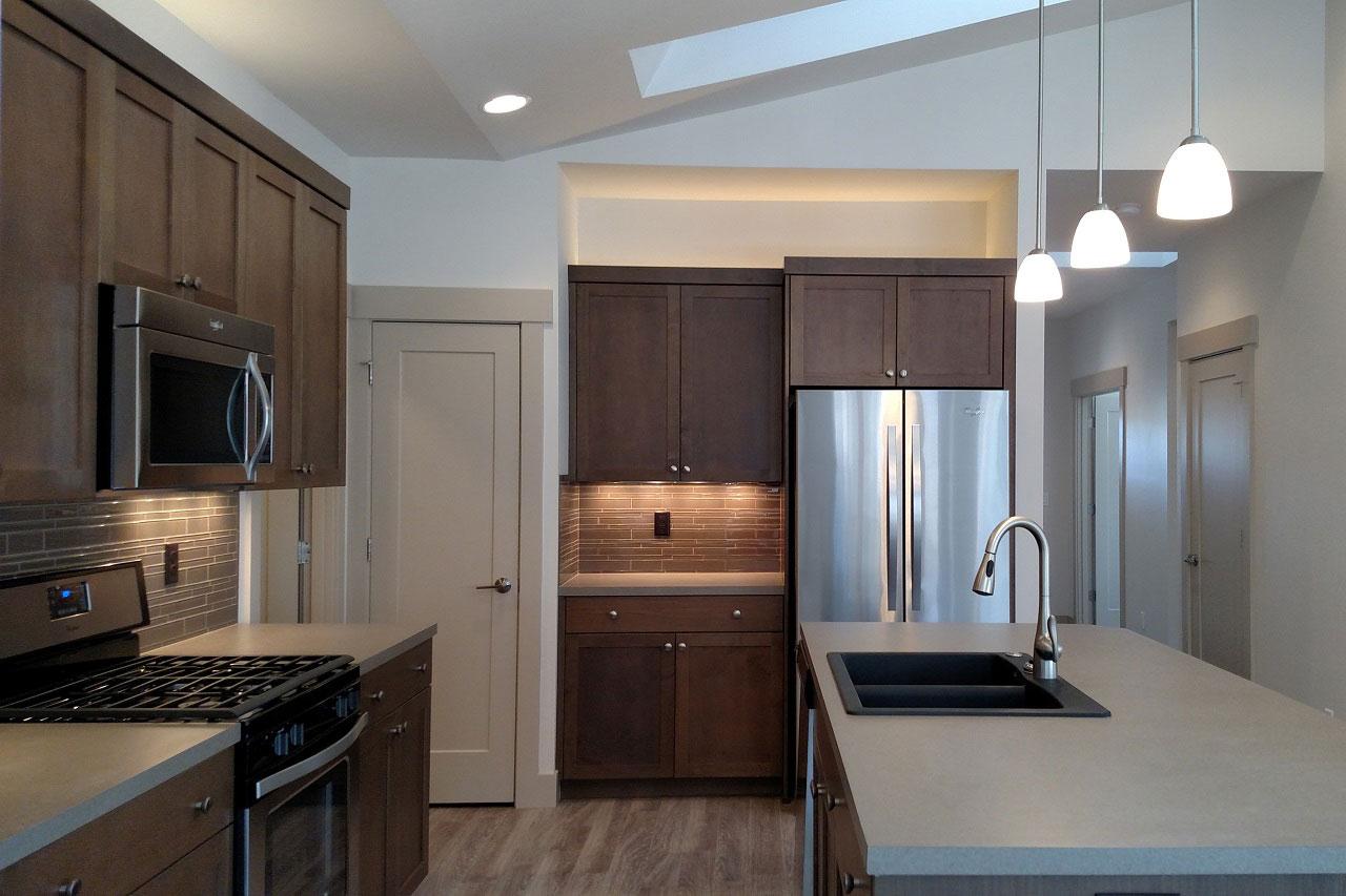 Kitchen with dark wood cabinets, stainless steel appliances, subway tile backsplash, and island with sink.