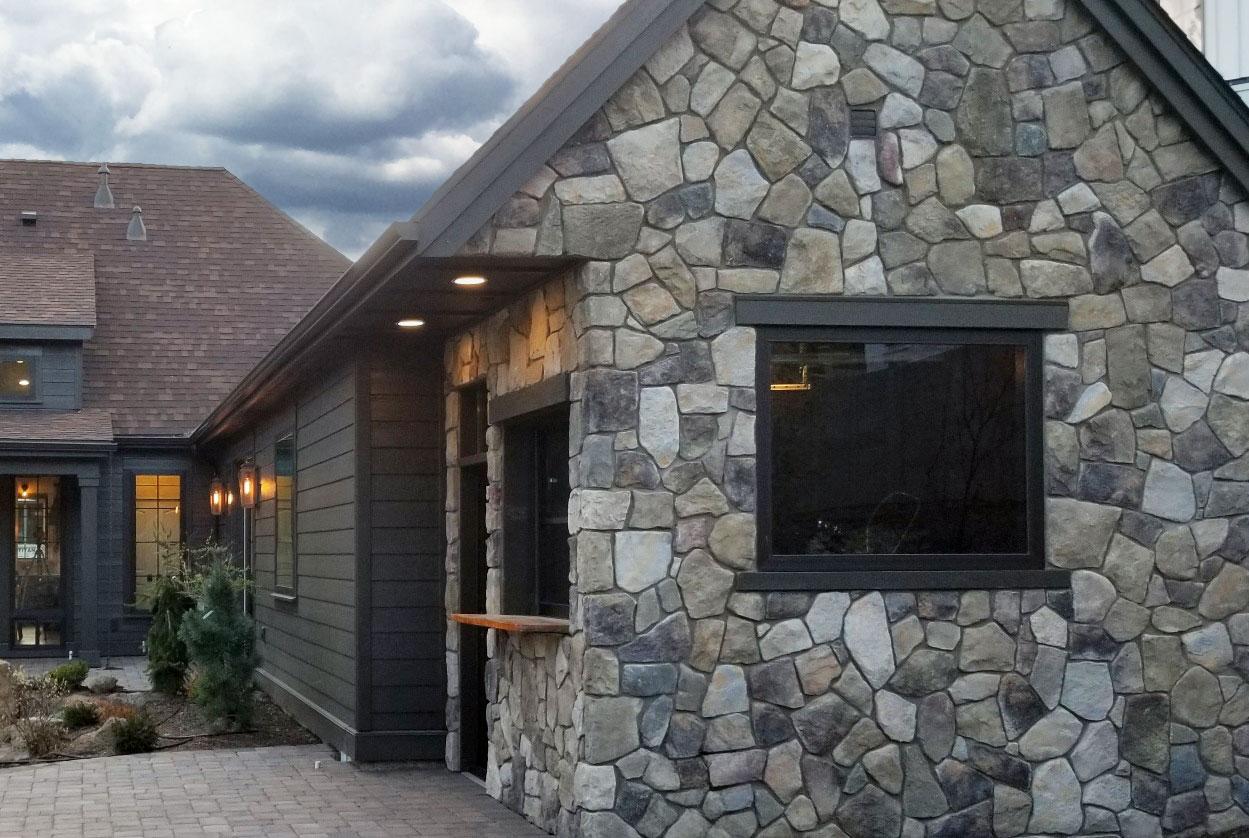 House plan exterior shows a stone facade with dark siding, gabled roof, and large windows.