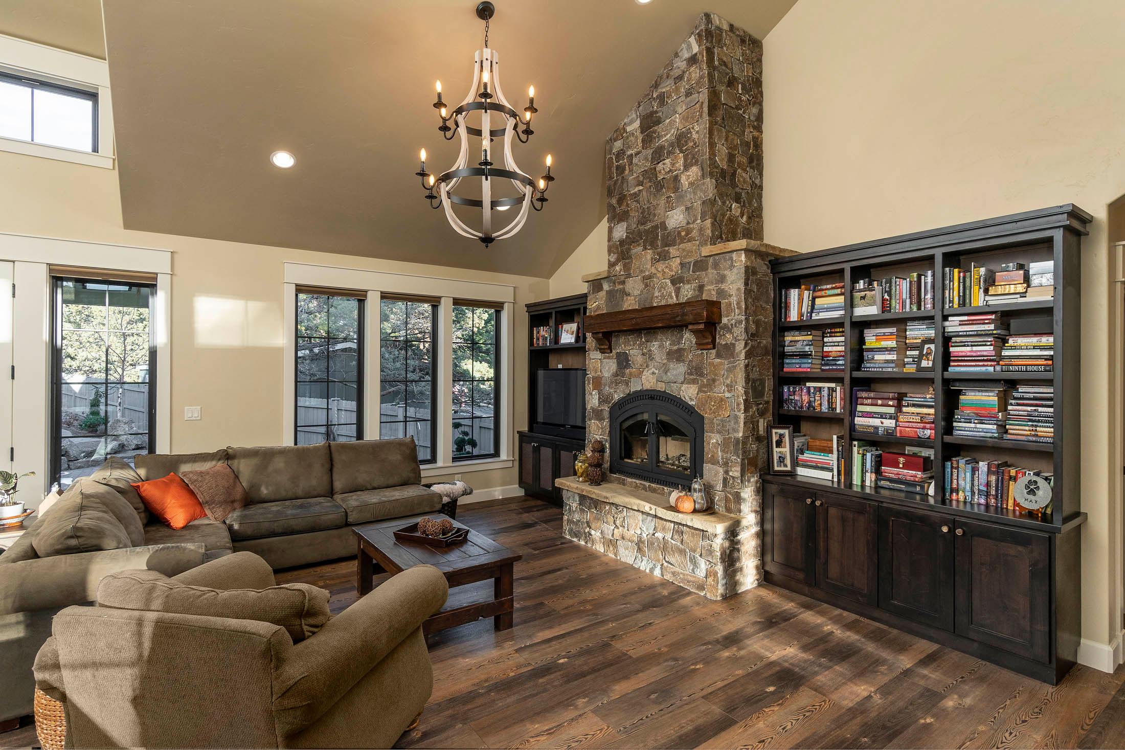 Living room interior with vaulted ceiling, stone fireplace, built-in bookshelves, and large windows.