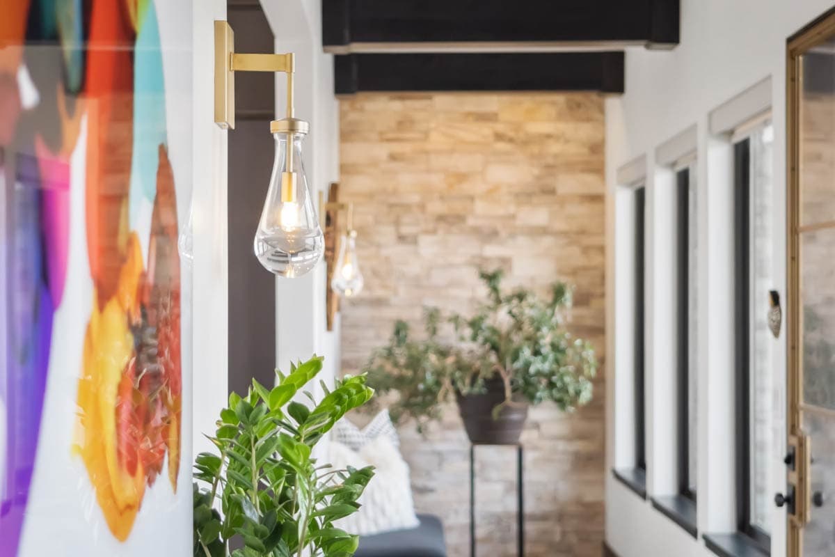 Interior hallway with modern brass sconces, stacked stone accent wall, and contemporary artwork.