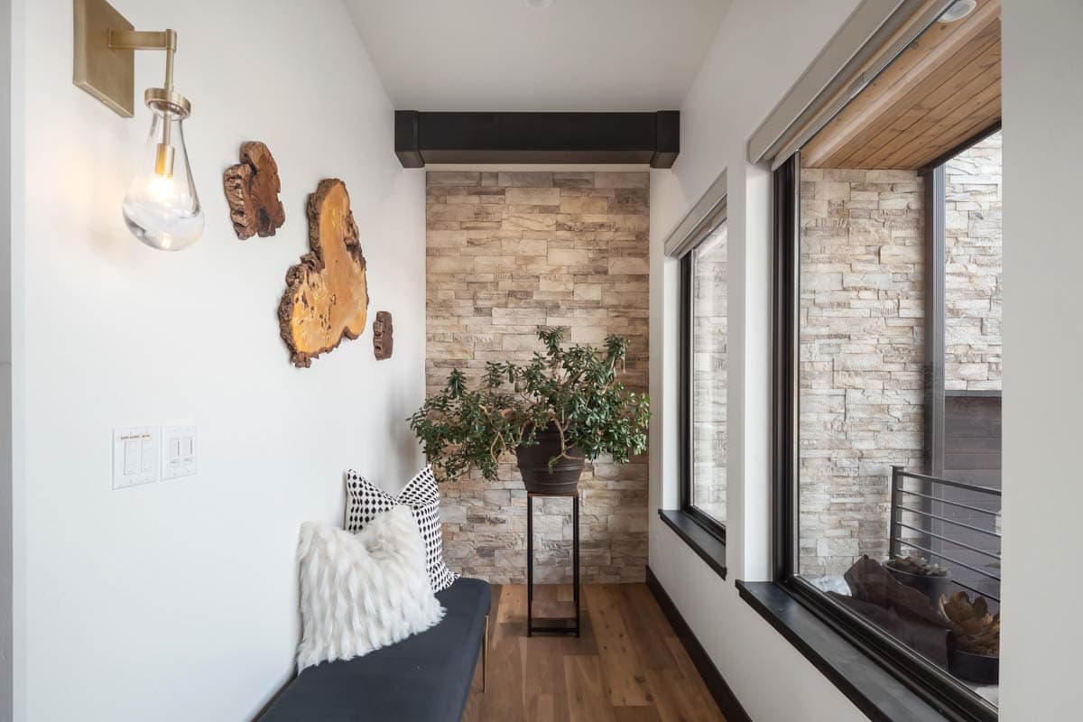 Interior view of hallway with stone accent wall, bench, wood floors, and large windows.