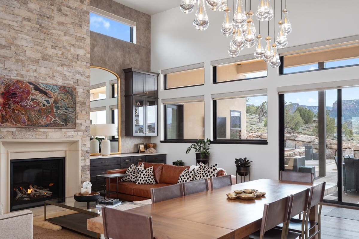 Living and dining area with stone fireplace, leather sofa, large windows, and wood dining table.