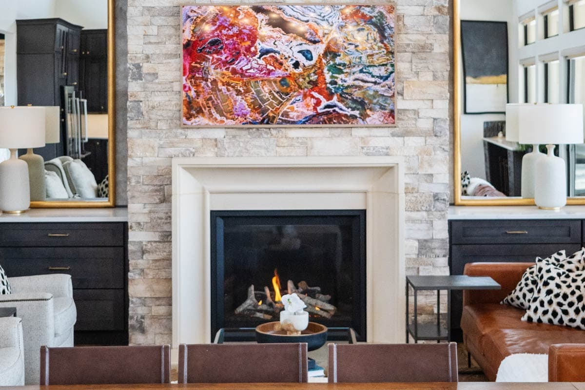 Living room with a stone fireplace, gas logs, flanked by dark cabinetry and gold-framed mirrors.