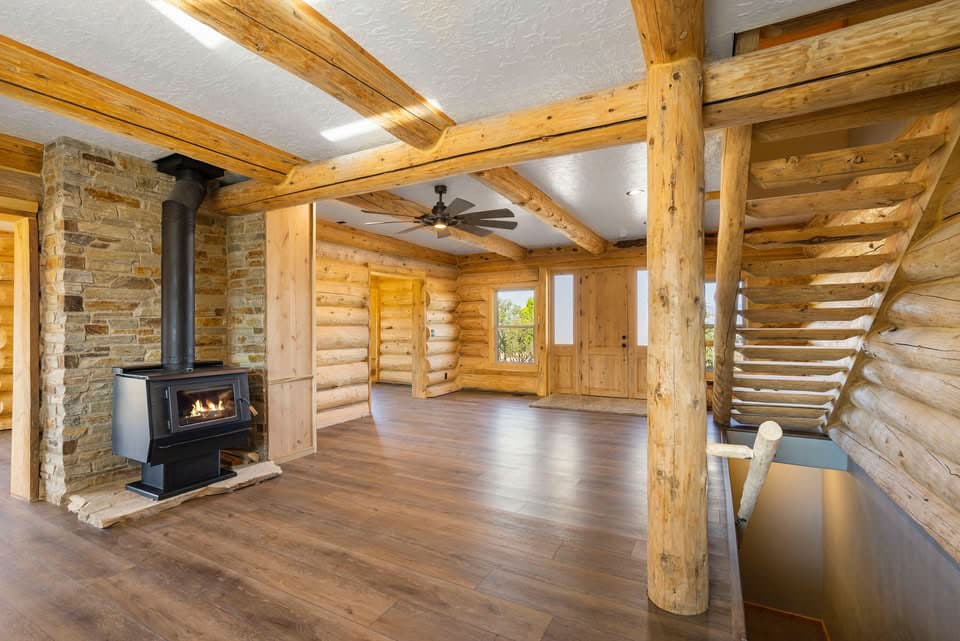 Log cabin interior featuring a stone fireplace, wood-beamed ceiling, staircase, and double doors.