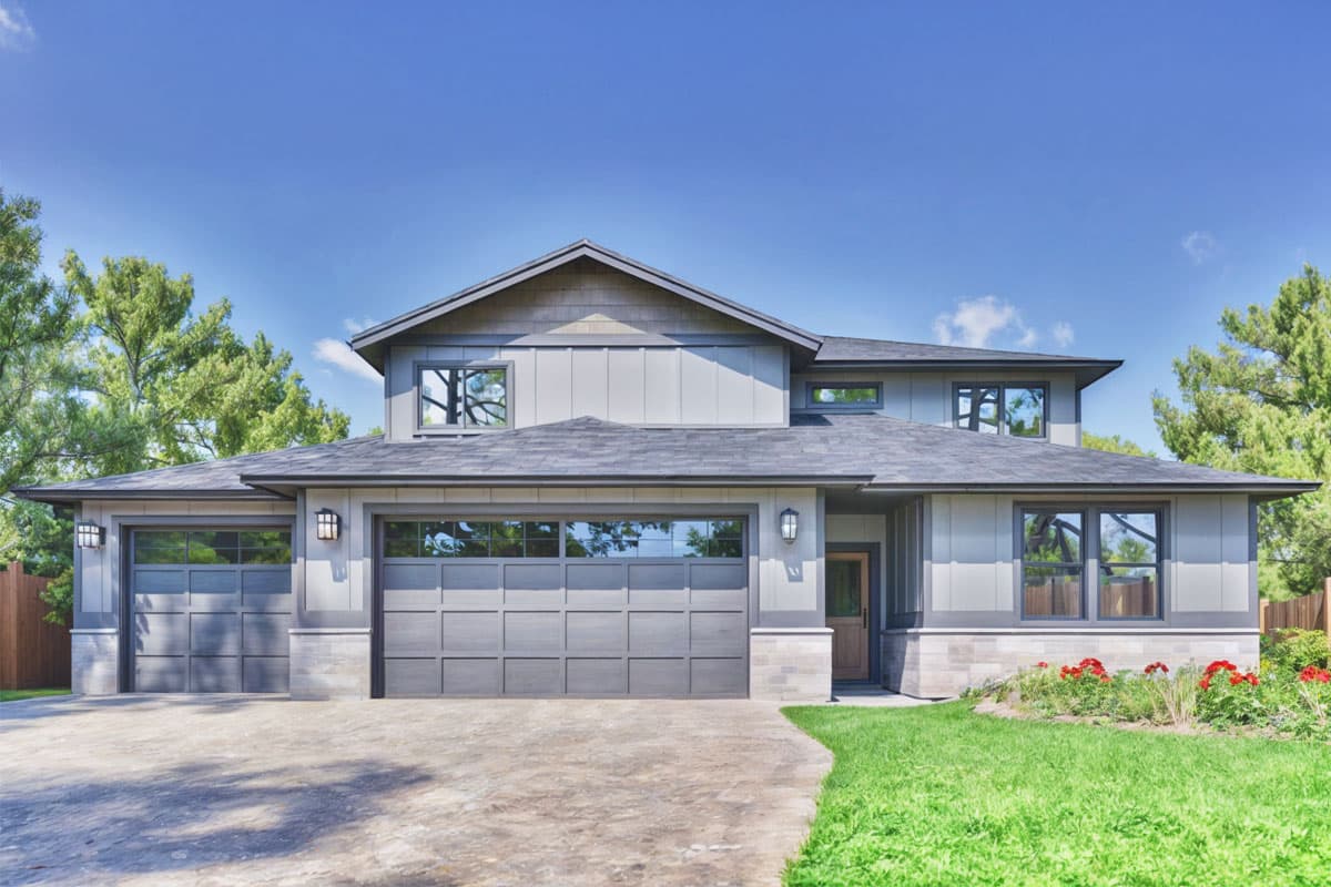 House plan exterior with two-car garage, multiple gables, and gray siding. Features include a covered entry and a combination of windows.