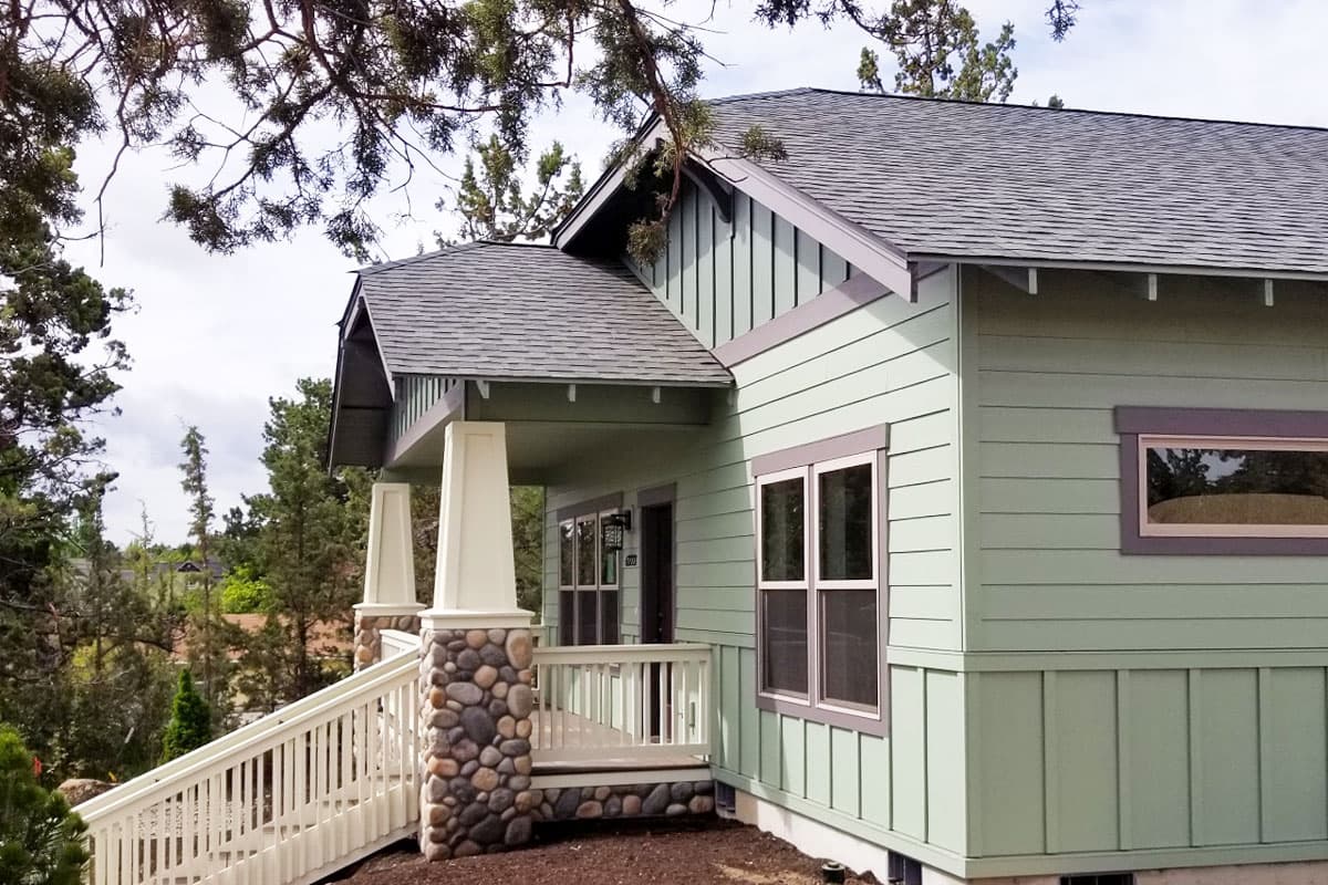 House plan exterior: Two-story home with gabled roof, covered porch with stone-clad columns, and double-hung windows.