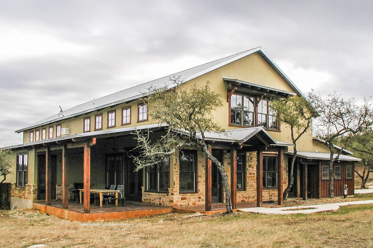 House plan exterior of a two-story home with stone base, wide covered porch, metal roof, and multiple gabled dormers.