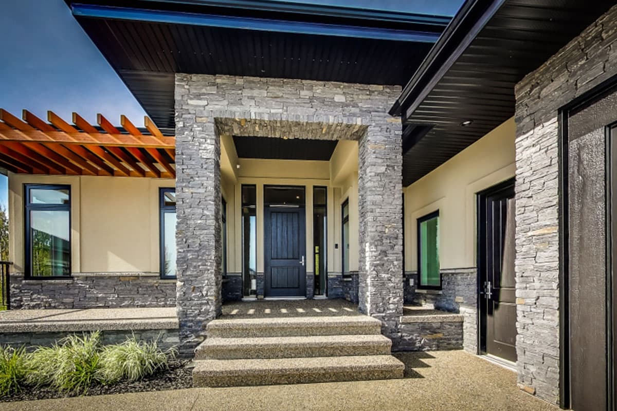Modern house plan exterior with stone facade, covered entryway, black door, and wood pergola.