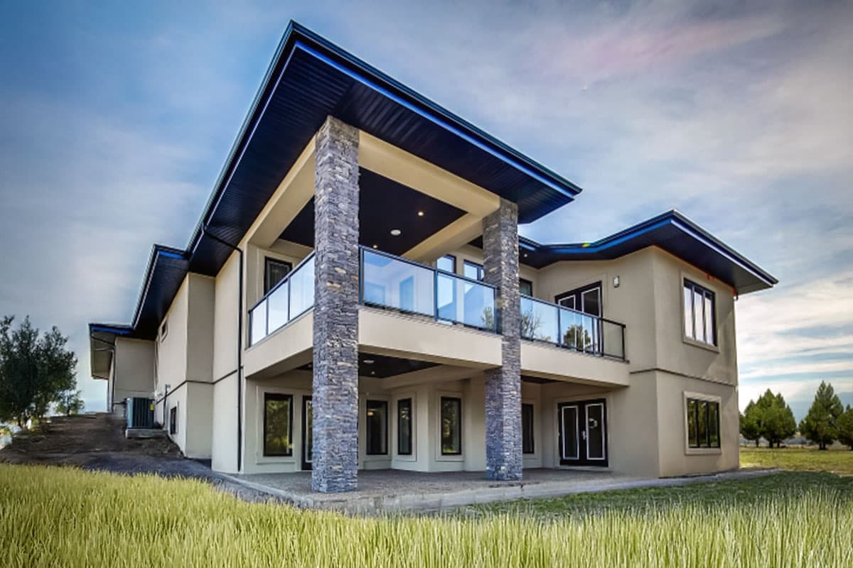 Modern house plan exterior with stone-clad columns, cantilevered upper deck with glass railings, and multiple stories.