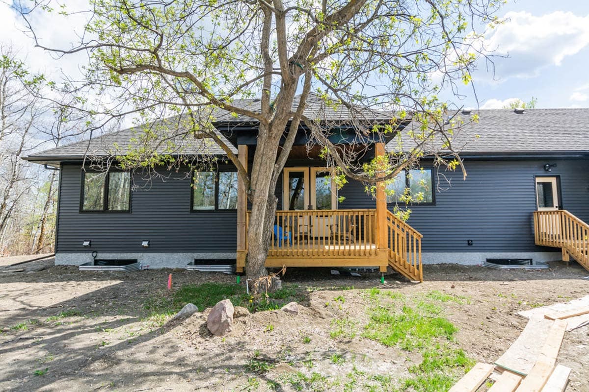 House plan exterior with dark siding, covered porch with wooden railings, and a gabled roof. Features a back door and windows.