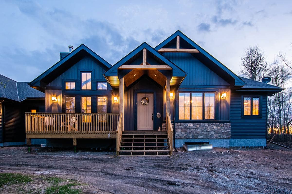Modern house plan exterior with dark siding, stone accents, gabled rooflines, prominent porch, and wooden deck.