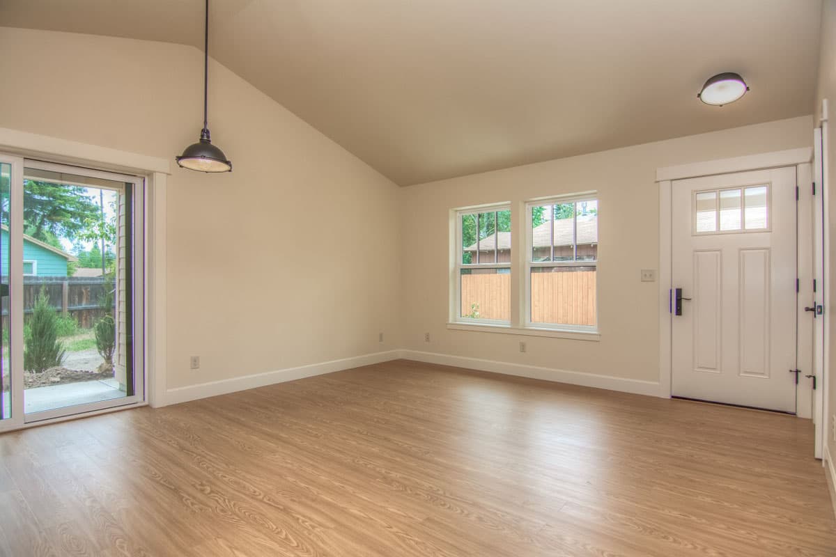 Interior view showing an empty room with a sliding glass door, two windows, a front door, and a vaulted ceiling.