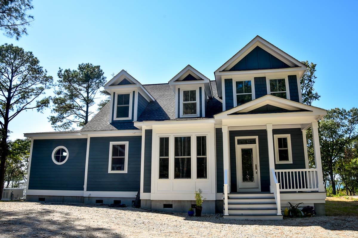 House plan exterior with a covered porch, multiple gables, dormers, and a circular window.