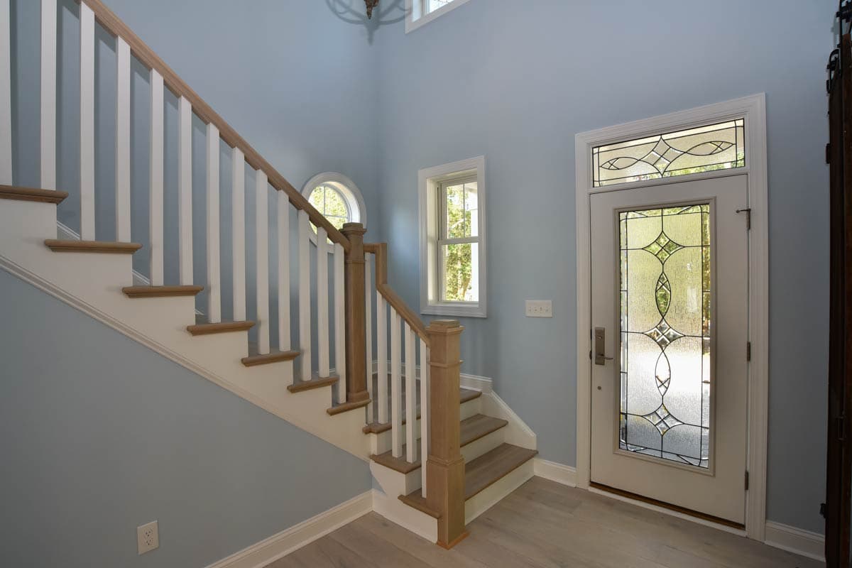 Interior view of foyer with wood and white staircase, round window, and entry door with decorative glass.