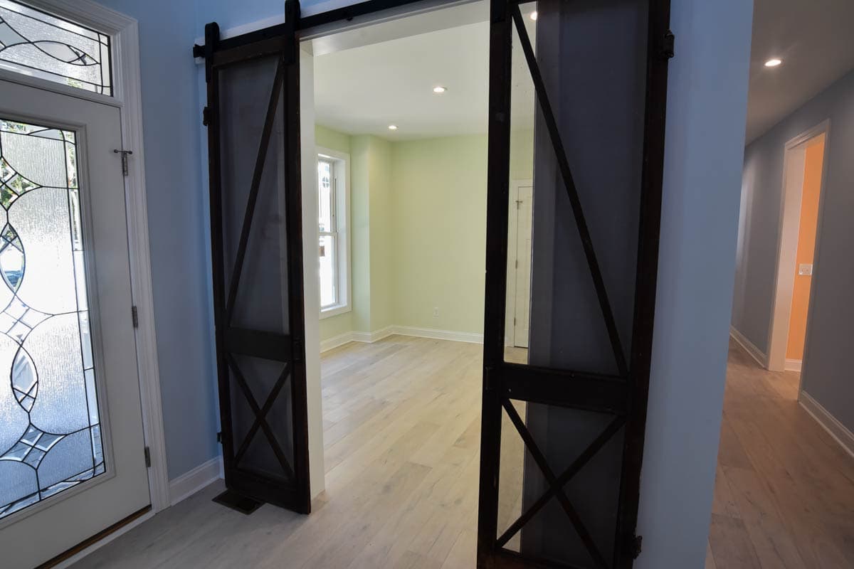 Interior view of entryway with decorative glass door, dark wood barn doors, and light wood flooring leading to a room with pale green walls.