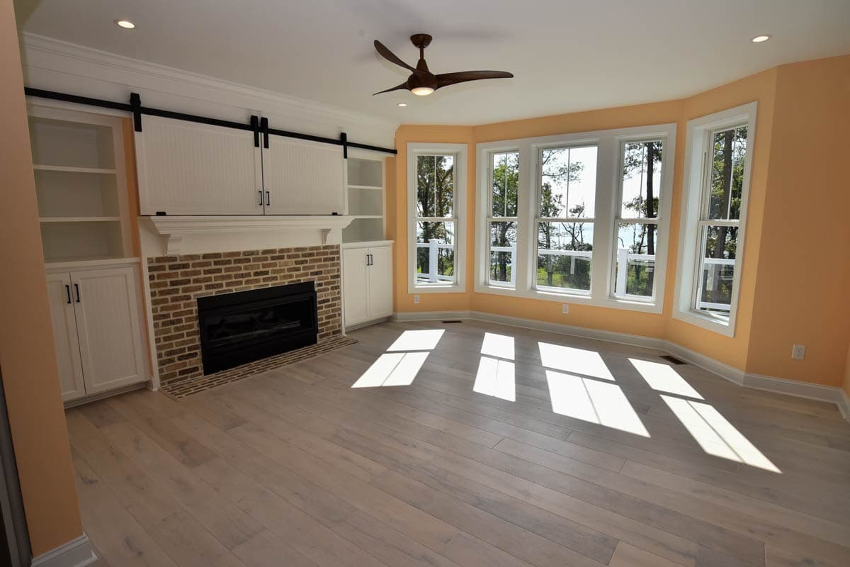 Living room with brick fireplace, white built-in cabinetry with barn doors, and bay windows.