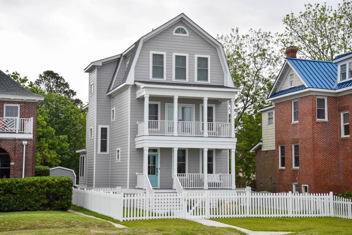 House plan exterior featuring a three-story design with a gambrel roof, two-story porch, and a white picket fence.