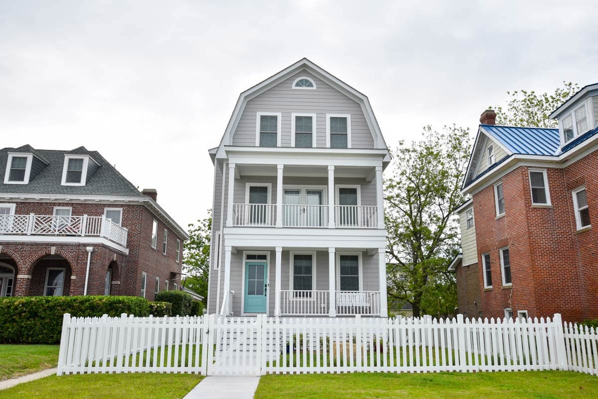 House plan exterior, three stories, gambrel roof, two front porches, white picket fence.