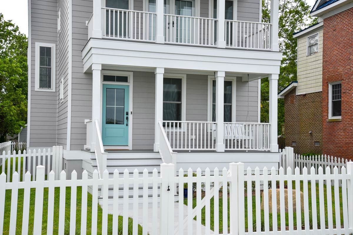 House plan exterior: Two-story home with a covered front porch, balcony, siding, and white picket fence.