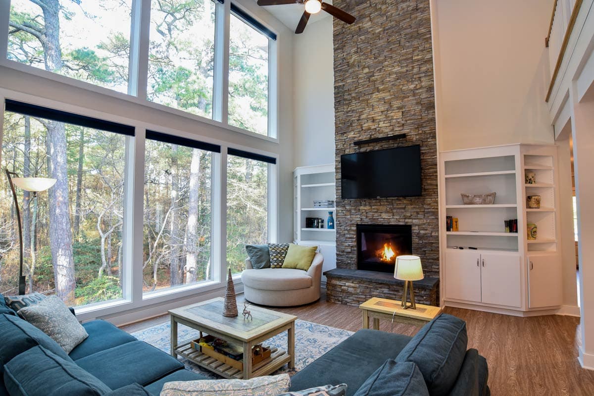 Living room with vaulted ceiling, stacked stone fireplace, wall of windows, and built-in shelving.