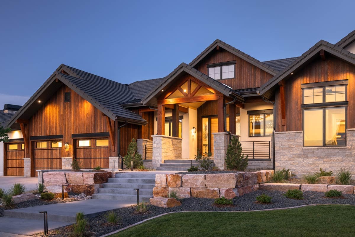 House plan exterior featuring a wood-clad facade, stone accents, prominent gables, a covered entry with exposed beams, and a three-car garage.