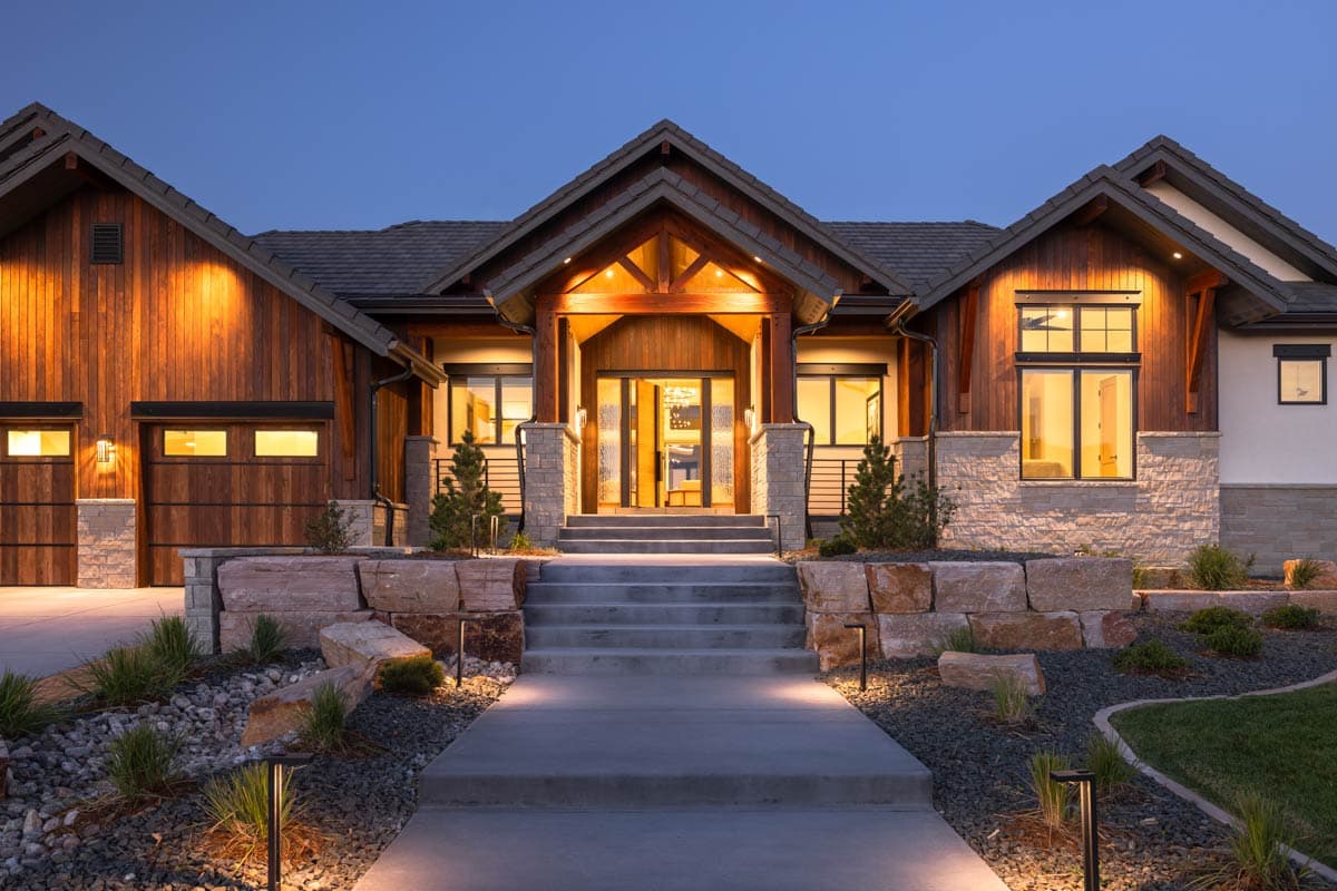 Modern mountain style house plan exterior with stone and wood siding, prominent gabled entrance, and attached garage.