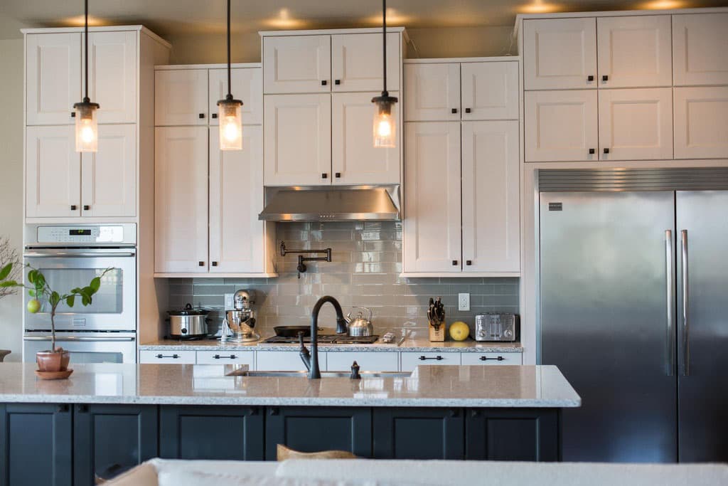 Kitchen with white cabinetry, stainless steel appliances including double ovens and refrigerator, subway tile backsplash, and a large island.