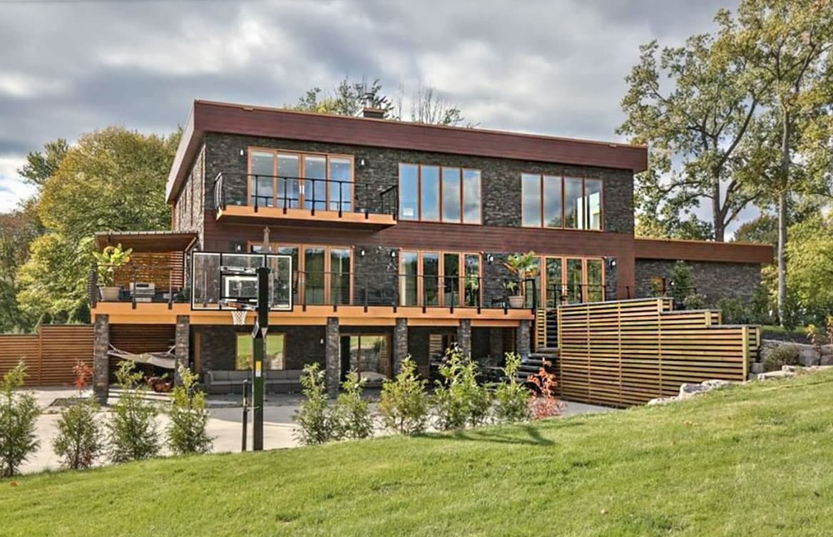 Modern house plan exterior with dark stone facade, multiple balconies, wood siding, and expansive windows.