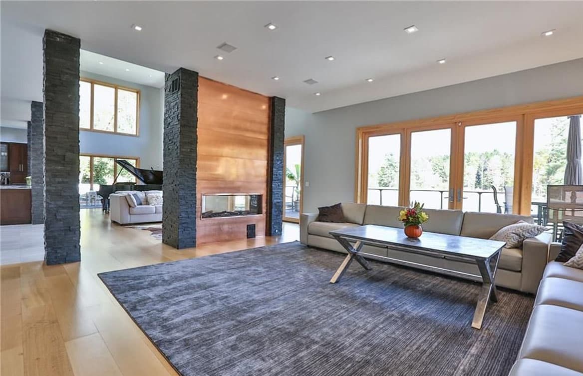 Open-concept living area with dual-sided fireplace, stone columns, and large windows.
