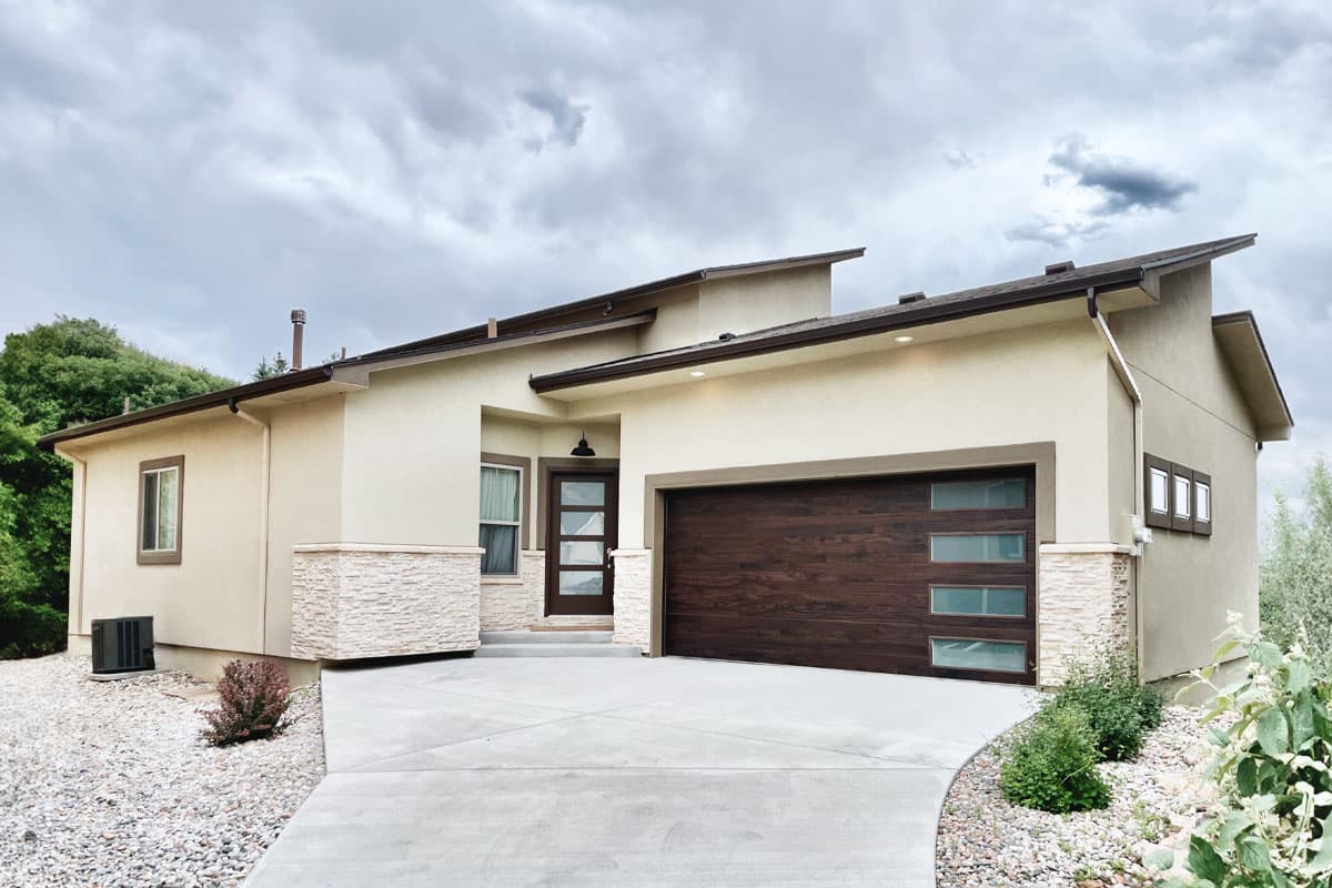 House plan exterior. Modern style, single story. Features include flat roof, stacked stone accents, and an attached garage with windows.