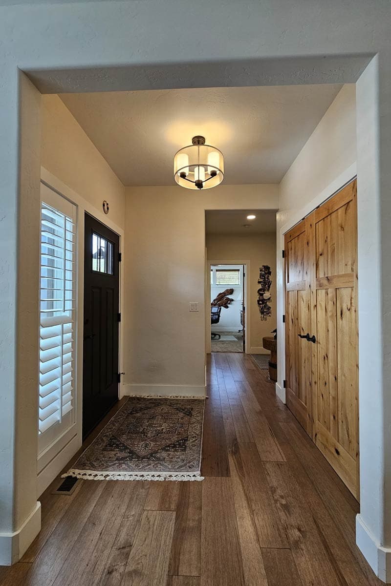 Interior view of a hallway with a dark front door, white louvered shutters, and knotty pine double doors.