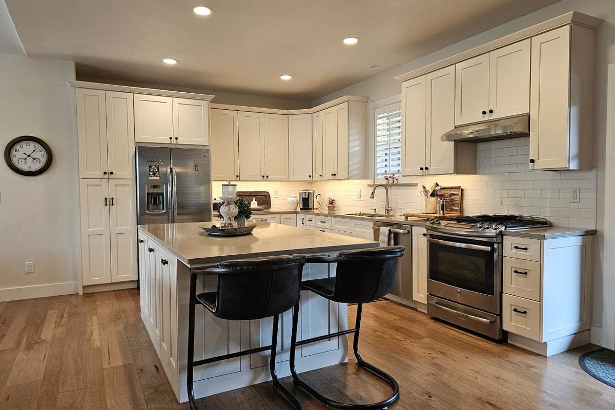 Kitchen with island, stainless steel appliances, white cabinets, subway tile backsplash, and hardwood floors.