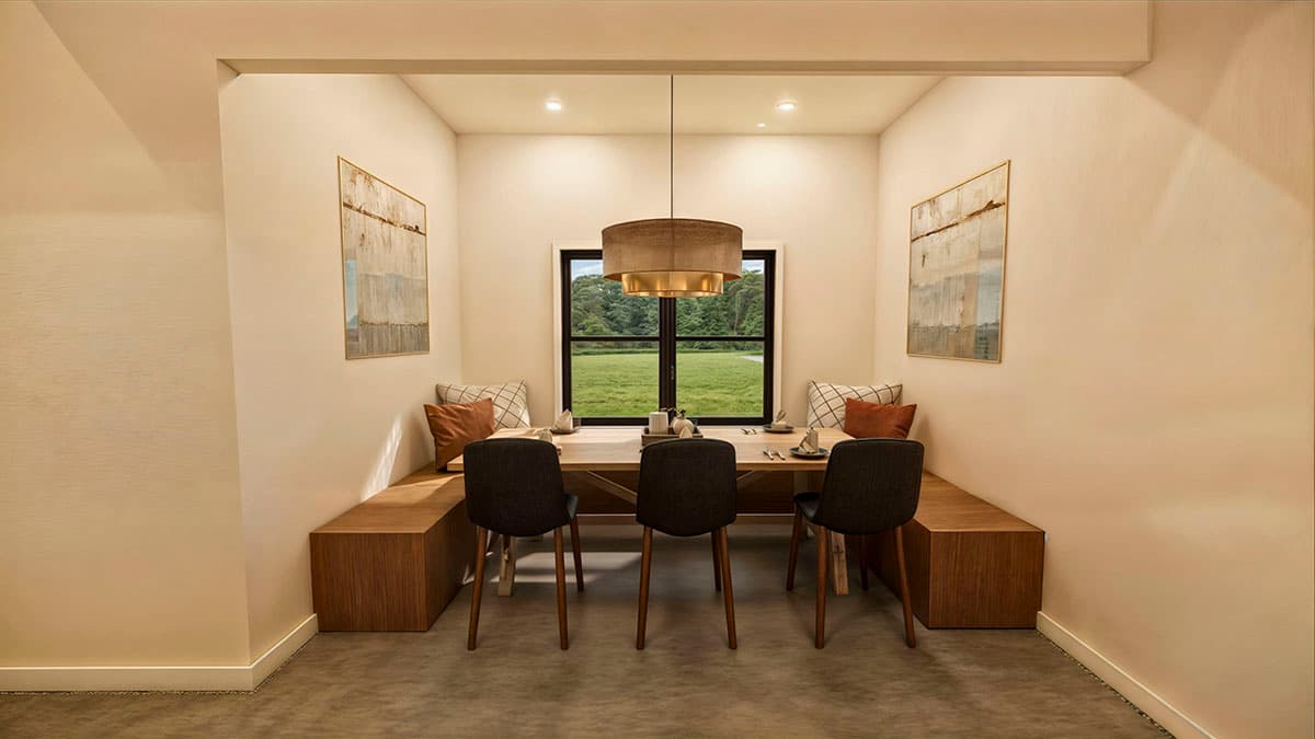 A dining room nook features a wooden table, bench seating, and chairs, with artwork on the walls and a large window overlooking a green field.