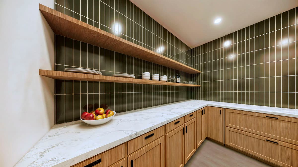 A modern pantry with wooden shelves, cabinets, and a marble countertop. A bowl of fruit sits on the counter, with plates and bowls on the shelves.