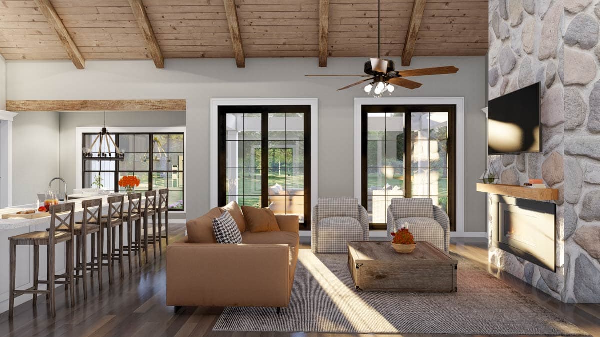Open-concept living area with wood-beamed ceiling, stone fireplace, kitchen island with bar seating, and large windows.