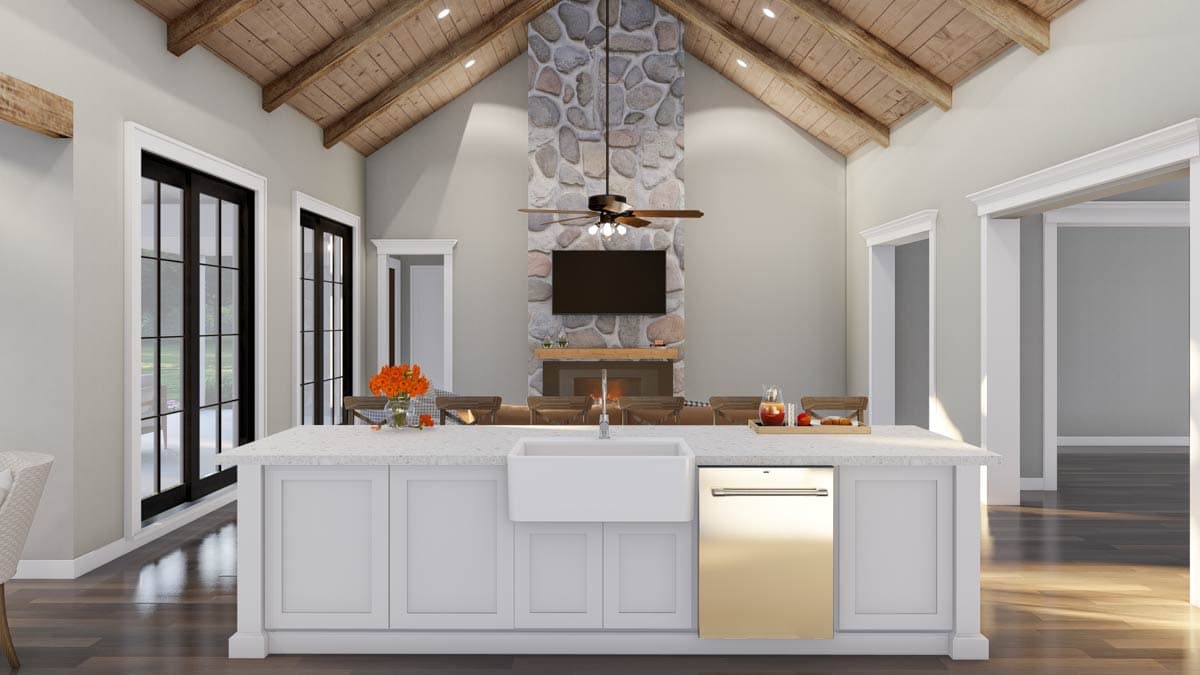 Great room interior with vaulted beam ceiling, stone fireplace with TV, large island with farmhouse sink, and black-framed doors.